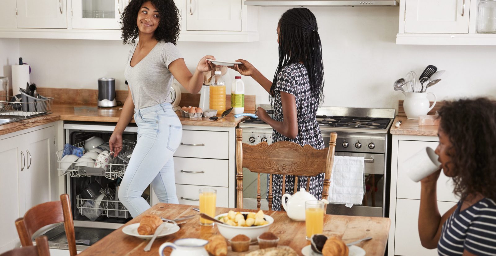 Three Teenage Girls Clearing Table After Family Breakfast